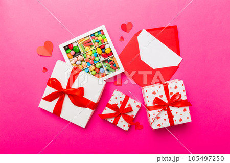 Red envelope with candy and gift box and Valentines hearts on colored background. Flat lay, top view. Romantic love letter for Holiday concept Red envelope with candy and gift box and Valentines hearts on colored background. Flat lay, top view. Romantic love letter for Holiday concept 105497250
