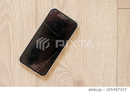 Smartphone with a broken touch screen, glass with cracks on wooden background. Mobile phone display crack mockup. Cellphone hit, crashed and scratch. Device destroyed. Electronic device repair 105497337