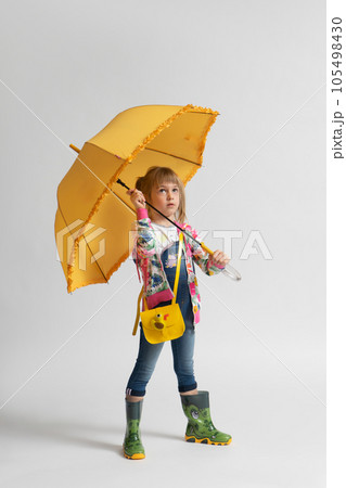 A girl in casual autumn clothes and rubber boots hides from the rain under an umbrella A girl in casual autumn clothes and rubber boots hides from the rain under an umbrella 105498430