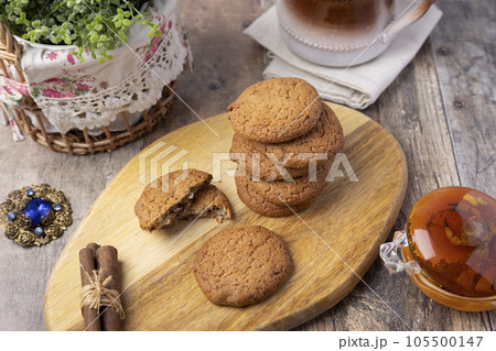 Oatmeal raisin cookies on a wooden board with cinnamon (cassia) sticks and a cup of milk. Traditional homemade pastry in rustic style. Selective focus, close-up. 105500147