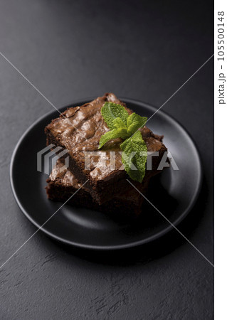 Chocolate brownie cake with mint. Traditional American dessert. Popular cake with dark chocolate on a black background. Close-up, selective focus. 105500148