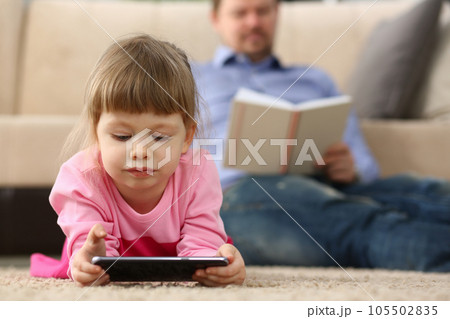 Man reads a book child plays with smartphone at home 105502835