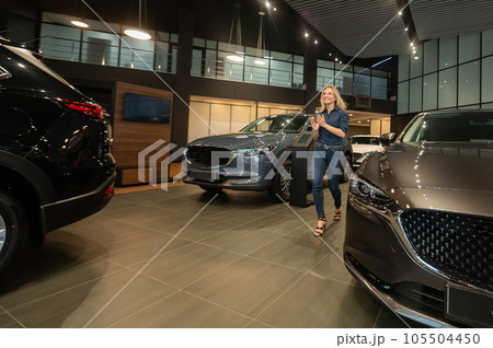 Young caucasian woman rejoices buying a car in a car dealership. Young caucasian woman rejoices buying a car in a car dealership. 105504450