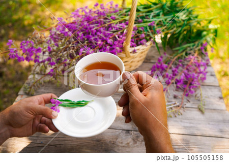 Close-up of men's hands with a white cup of tea. Healthy organic leaves Ivan chai tea Russian herbal on the wooden table 105505158