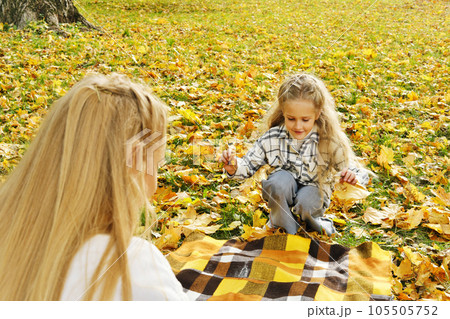 The family has fun in the park. Girl and mother spread a plaid on an autumn meadow The family has fun in the park. Girl and mother spread a plaid on an autumn meadow 105505752