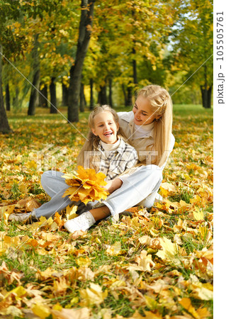 The family has fun in the park. Girl and mother sit on the ground among yellow leaves and fool around The family has fun in the park. Girl and mother sit on the ground among yellow leaves and fool around 105505761