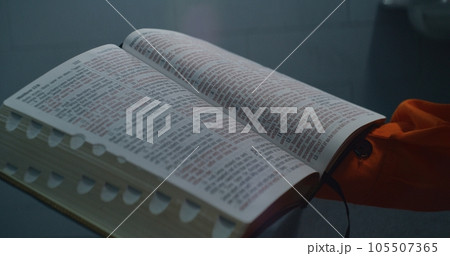 Prisoner in orange uniform reads Bible in prison cell 105507365