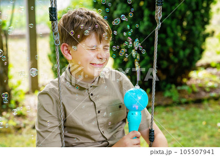 Happy little blonde preschool girl having fun with blowing soap bubble blower. Cute child playing on sunny summer day. Happy active funny healthy kid. Activity for children. 105507941