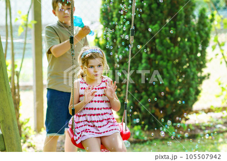 Happy little preschool girl and school kid boy having fun with blowing soap bubble blower. Children, lovely siblings playing together. Active funny healthy kids. Brother and sister in love. 105507942