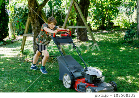 Happy preteen kid boy with lawn mower. Portrait of smiling teenager child working in garden, trimming grass. Garden works in summer. Kid helping 105508335