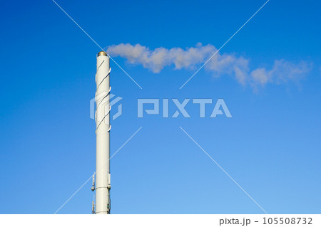 A tall white smoking chimney against a blue sky background 105508732