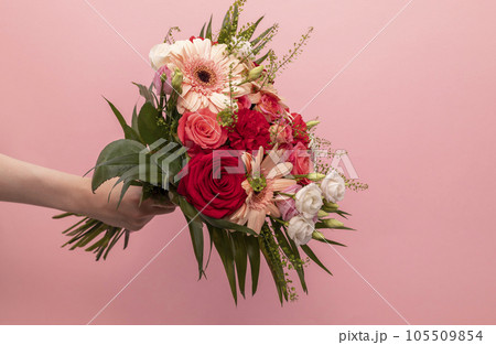 Real Human Hand Holding Beautiful Fresh Bouquet Of Flowers For Bride Or Occasion On Pink Background. Colorful Mixed Roses, Carnation Shabot, Green Leaves, Gerber. Horizontal Plane, Copy Space 105509854
