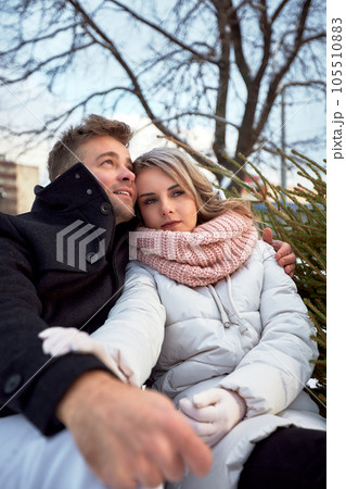 Happy couple in love in Christmas market. Young beautiful man and woman in winterwear embracing and looking dreamily into the distance. Romantic outside dating in winter snowy city. 105510883