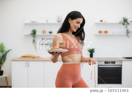 Happy woman measuring waist with tape after workout at home 105511403