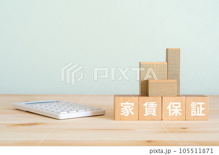 家賃保証と書かれたブロック、電卓、ミニチュアの建物 家賃保証と書かれたブロック、電卓、ミニチュアの建物 105511871