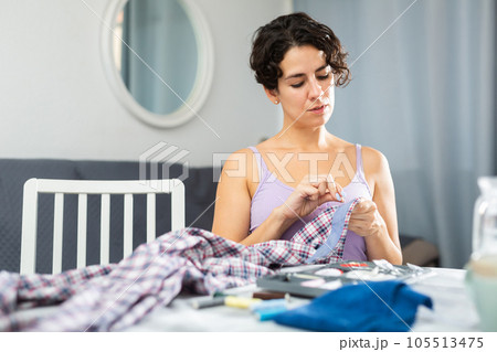 Portrait of attractive focused female using needle and thread to sew shirt 105513475