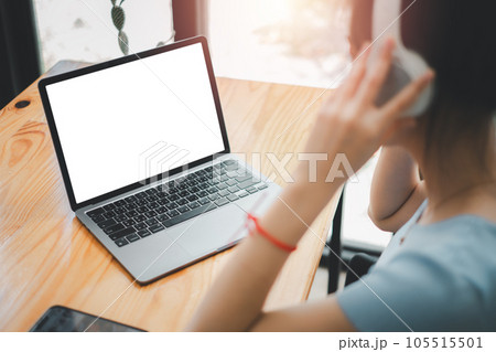 Close-up back view of a woman working on notebook computer and using headphone, looking at the screen. office worker using a notebook computer.. Close-up back view of a woman working on notebook computer and using headphone, looking at the screen. office worker using a notebook computer.. 105515501