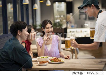 ビールのジョッキを運ぶホールスタッフとテーブル席の若い男女のグループ ビールのジョッキを運ぶホールスタッフとテーブル席の若い男女のグループ 105516035