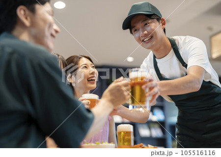 テーブルのお客さんにビールのジョッキを手渡すホールスタッフ　 105516116