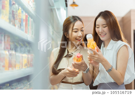 Two beautiful Asian women shopping and checking items in supermarket. Female friends meeting and examining nutrition labels at convenient store 105516719