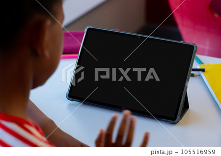 Biracial schoolgirl waving hand and having tablet video call with copy space 105516959