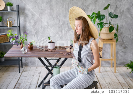 Portrait of Woman gardener transplanting plants. Concept of home garden. Flower and garden shop. A straw hat with a wide brim. Portrait of Woman gardener transplanting plants. Concept of home garden. Flower and garden shop. A straw hat with a wide brim. 105517353