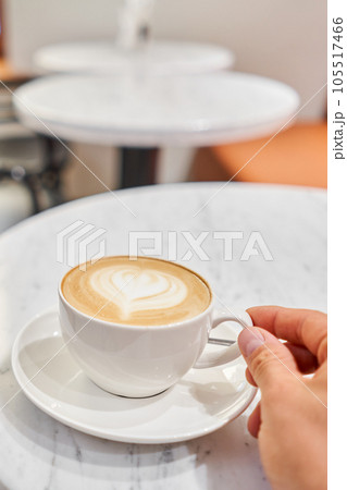 A man holds a cup with his hand A cup of hot cappuccino on the table in the coworking space of the coffee shop. Coffee break at the cafe. Close-up 105517466