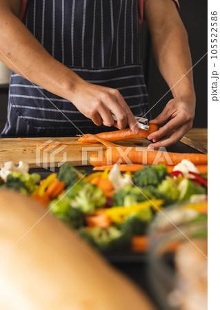 Midsection of biracial man in apron peeling carrot on chopping board, copy space Midsection of biracial man in apron peeling carrot on chopping board, copy space 105522586