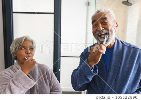 Portrait of happy senior biracial couple wearing bathrobes and brushing teeth in bathroom at home 105522890
