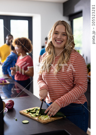 Portrait of happy caucasian woman cutting vegetables with diverse friends in kitchen 105523281