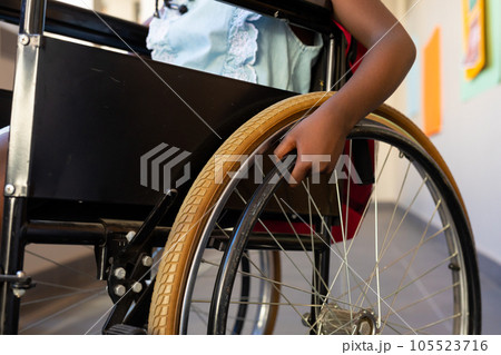 Mid section of african american schoolgirl sitting in wheelchair at elementary school corridor 105523716