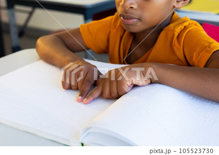 Focused biracial schoolboy reading braille with hands in classroom Focused biracial schoolboy reading braille with hands in classroom 105523730
