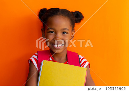 Portrait of happy african american schoolgirl with books over orange background at elementary school 105523906