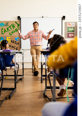 Diverse happy male teacher with tablet and elementary schoolchildren sitting at desks in class Diverse happy male teacher with tablet and elementary schoolchildren sitting at desks in class 105523907