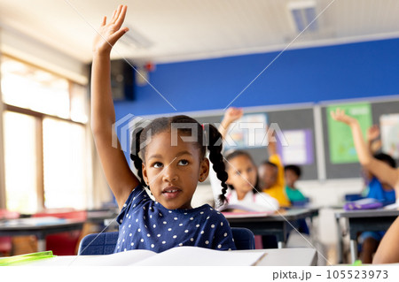 Diverse elementary schoolchildren sitting at desks and raising hands in class Diverse elementary schoolchildren sitting at desks and raising hands in class 105523973