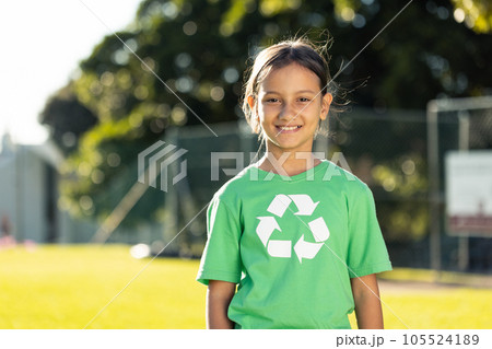 Happy biracial schoolgirl wearing green recycling tshirt in elementary school on sunny day Happy biracial schoolgirl wearing green recycling tshirt in elementary school on sunny day 105524189