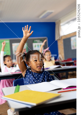 Diverse elementary schoolchildren sitting at desks and raising hands in class Diverse elementary schoolchildren sitting at desks and raising hands in class 105524206