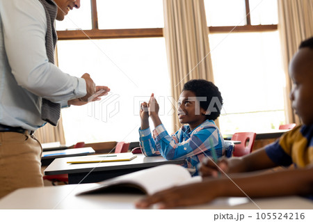 Diverse male teacher teaching school boy using sign language in class at elementary school 105524216