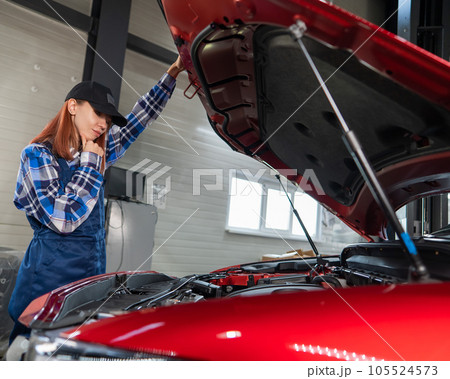 Woman auto mechanic opens the hood of a car in a car service.  105524573
