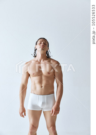 Portrait of handsome man with braids, muscular strong body standing shirtless in underwear against grey studio background 105526533