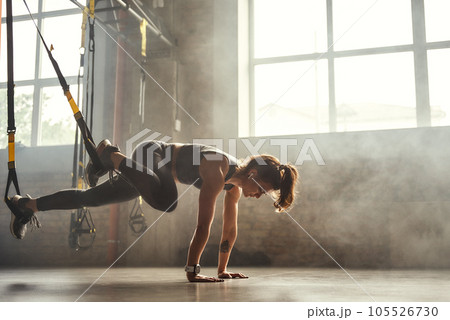 TRX Training. Young athletic woman in sports clothing training legs with trx fitness straps in the gym. TRX Training. Young athletic woman in sports clothing training legs with trx fitness straps in the gym. 105526730