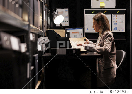Manager organizing corporate depository, analyzing accountancy report checking administrative record. Businesswoman reading bookkeeping documents, working late at night in storage room Manager organizing corporate depository, analyzing accountancy report checking administrative record. Businesswoman reading bookkeeping documents, working late at night in storage room 105526939