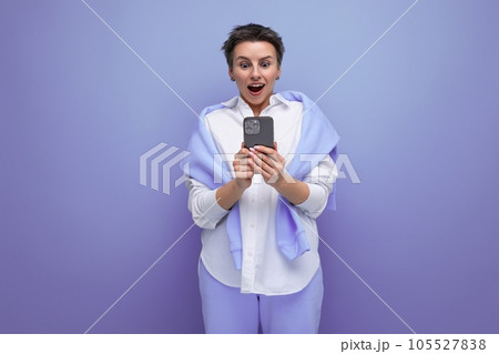 energetic positive young brunette woman with short haircut in white shirt chatting in smartphone 105527838