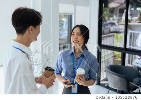 two young asian businesswomen standing chatting talking and holding coffee by the window in office 105528876