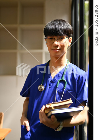 Portrait of medical student man wearing blue scrubs with stethoscope standing near window at campus Portrait of medical student man wearing blue scrubs with stethoscope standing near window at campus 105528965