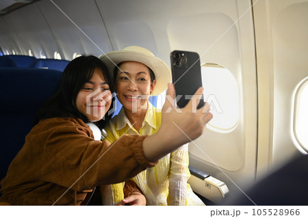 Smiling middle aged woman and daughter sitting in passenger airplane and taking picture, waiting for airplane landing 105528966