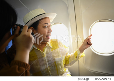 Smiling middle aged woman and daughter sitting in passenger airplane and taking picture, waiting for airplane landing 105528974