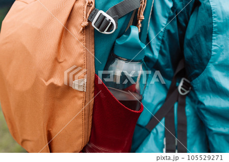 Close up of woman with water bottle in backpack pocket. Travel, tourism, hike and people concept. Rear view of male backpackers walking in field 105529271
