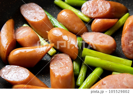ウインナーソーセージとにんにくの芽をフライパンで炒める調理シーン。 105529802