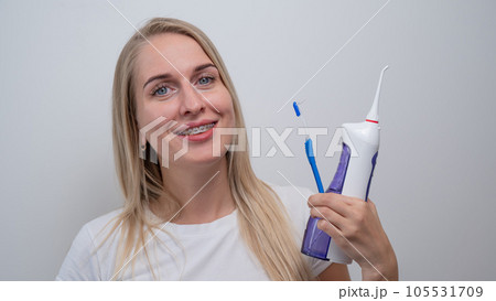Smiling caucasian woman with braces on her teeth holding an irrigator and a toothbrush. 105531709